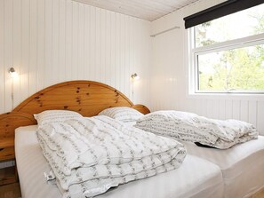 Una cama con cabecera de madera, ropa de cama blanca y dos lámparas fijadas a la pared.