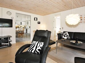 A modern living room with a leather chair, a black sofa, a dining table, and a kitchen in the background. - Luxury Holiday Home in Hadsund near Sea (Hadsund)