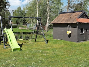A playground with a green slide and swings, a small shed, and a grassy area with trees. - Luxury Holiday Home in Hadsund near Sea (Hadsund)