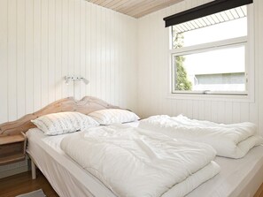 A bedroom with a wooden headboard, two beds with white bedding, a nightstand, a lamp, and a window with a view. - Luxury Holiday Home in Hadsund near Sea (Hadsund)