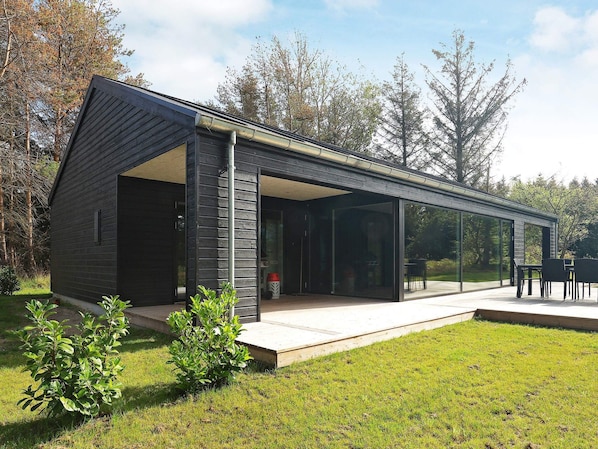 Uma casa moderna com uma ampla extensão de vidro, um pátio e um gramado bem cuidado.