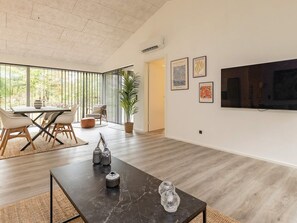 A modern living room with a dining area, a large window, and a flat-screen TV mounted on the wall. - 5 Star Holiday Home in Hjorring (Hjørring)