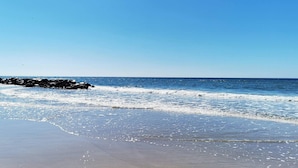 A beach with waves, a clear sky, and a rocky shoreline.