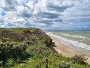 A coastal landscape with a lighthouse on a grassy hill, a sandy beach, and the ocean.
