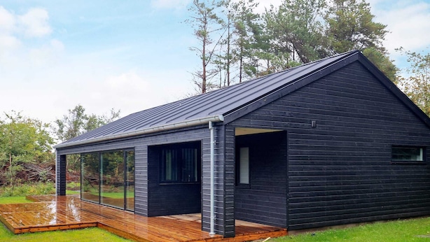 A modern house with a large glass window, a wooden deck, and a grassy yard.