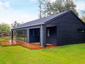 A modern house with a large glass window, a wooden deck, and a grassy yard.