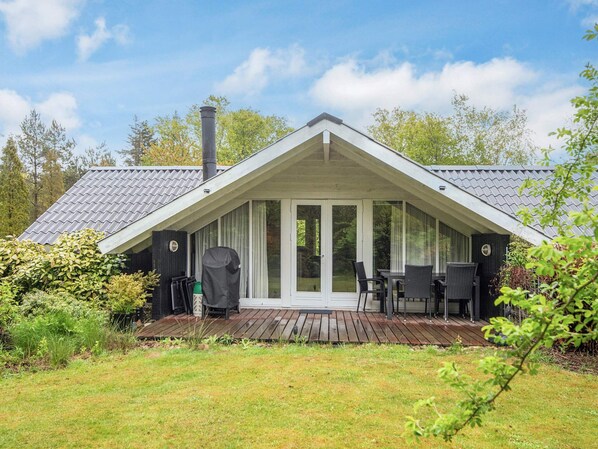 A modern house with a sloped roof, a covered porch with a table and chairs, and a chimney.