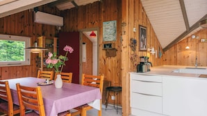 A wooden interior with a dining table, chairs, a kitchen area, and a window with a view of greenery. - 6 Person Holiday Home in Oksbol (Oksbol)
