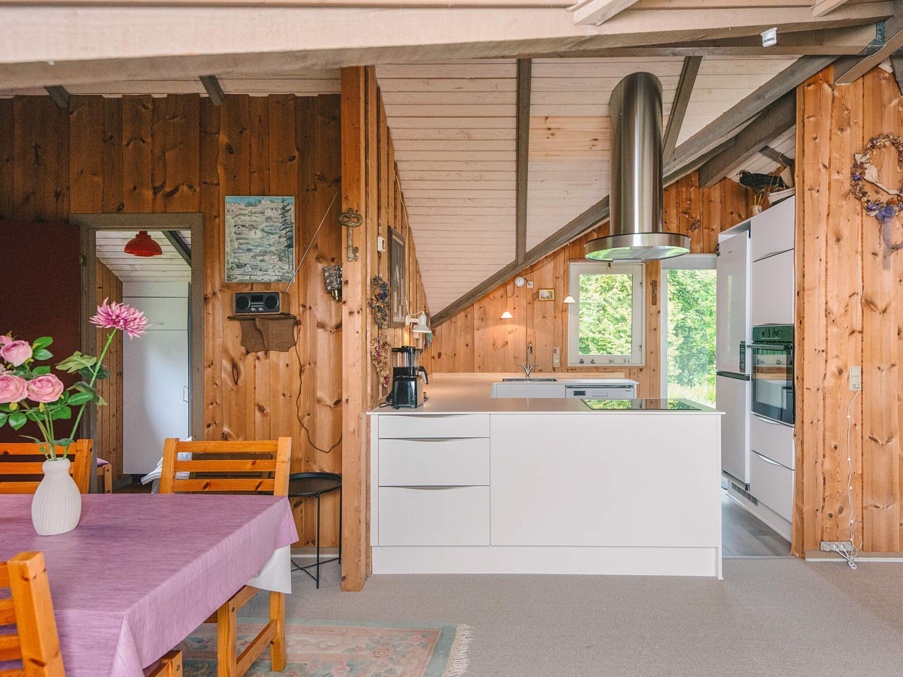 Interior de madera con cocina, mesa de comedor y sillas, y ventana con vistas a zonas verdes.