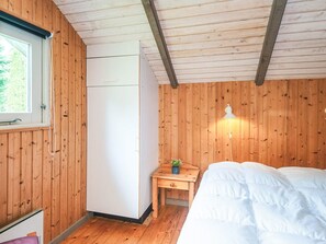 A room with wooden walls, a bed, a small table with a plant, a white lamp, and a window. - 6 Person Holiday Home in Oksbol (Oksbol)