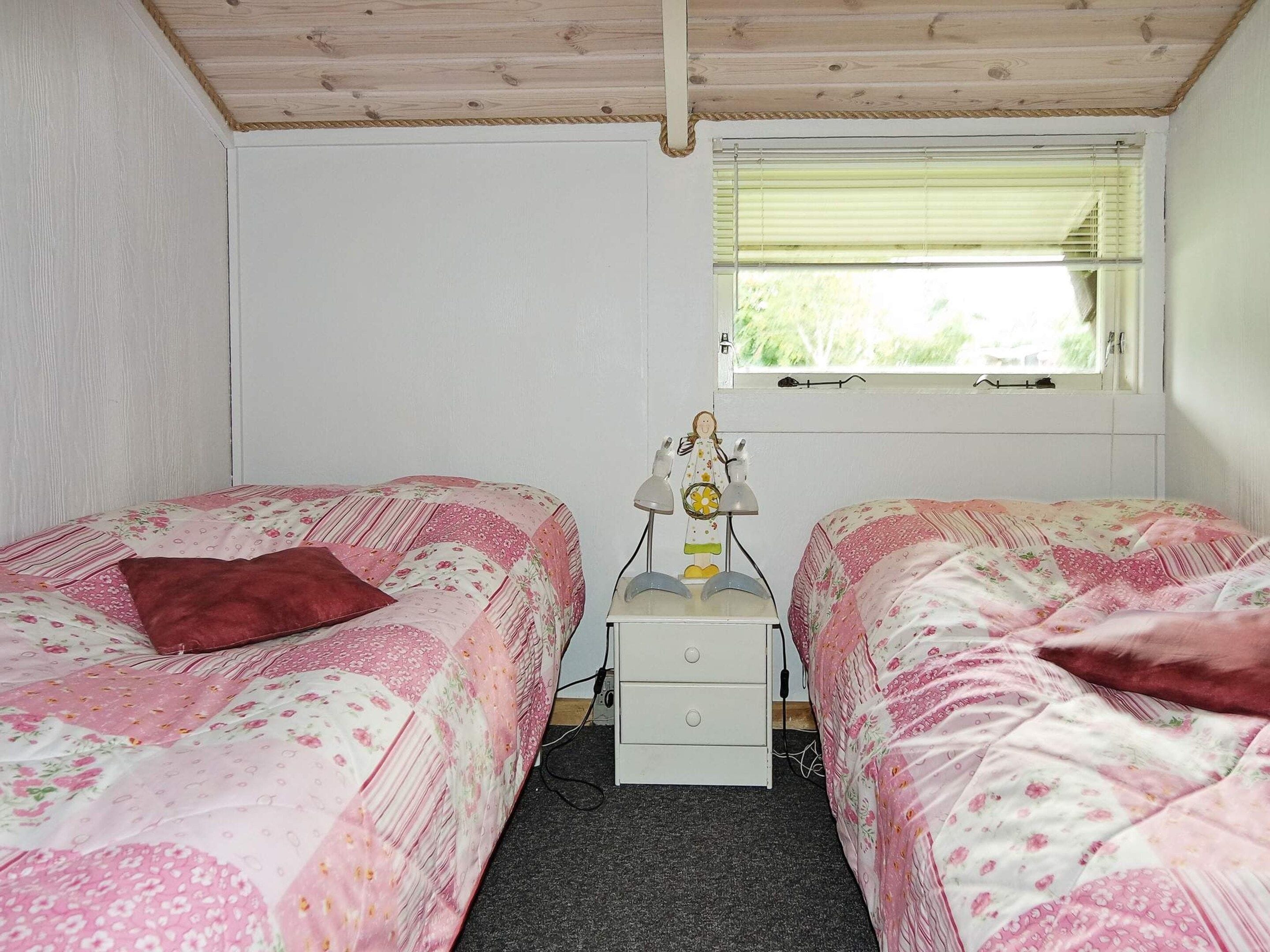 A bedroom with two single beds, a nightstand, a lamp, and a window with blinds.