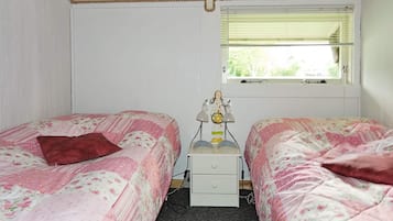 A bedroom with two single beds, a nightstand, a lamp, and a window with blinds.