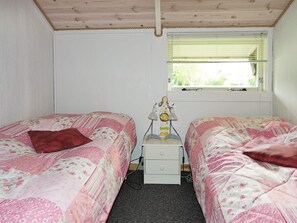 Ein Schlafzimmer mit zwei Einzelbetten, einem Nachttisch, einer Lampe und einem Fenster mit Jalousien.
