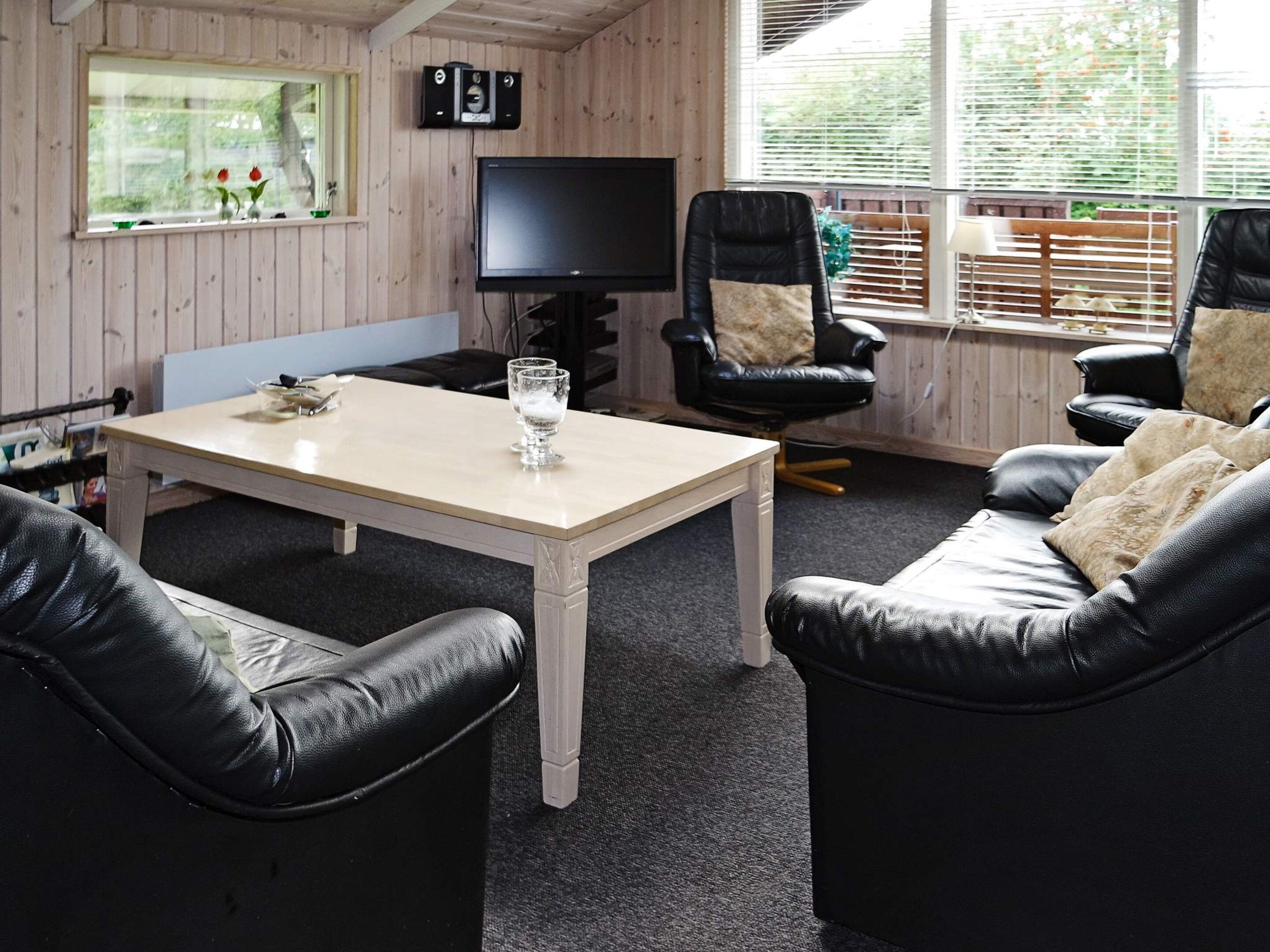 Et værelse med fjernsyn, to læderstole, en sofa, et bord og et vindue med skodder.
