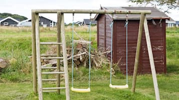 A wooden swing set with a ladder, a small shed, and a grassy field with houses in the background.