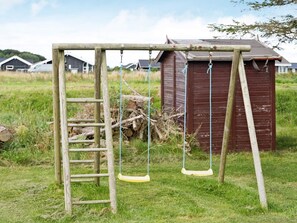 Eine Holzschaukel mit einer Leiter, eine kleine Gartenhütte und ein Wiesenfeld mit Häusern im Hintergrund.
