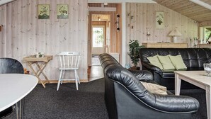 Et hyggeligt værelse med en sort lædersofa, et hvidt bord, en lille hvid stol og en trævæg med indrammede billeder.