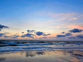 Una playa con olas, cielo despejado y nubes dispersas.