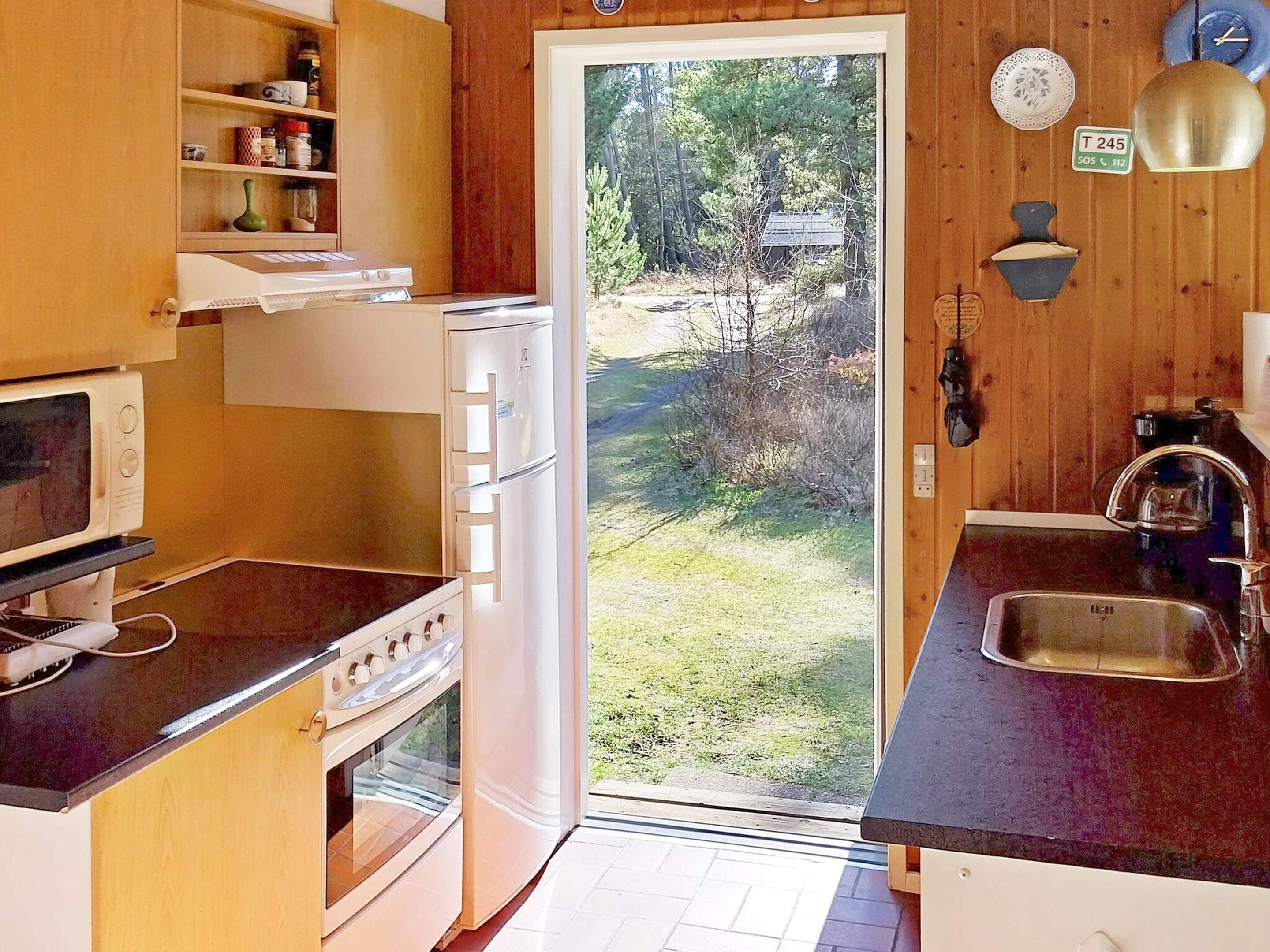A compact kitchen with a microwave, stove, and sink, wooden cabinets, and a door leading to a backyard.