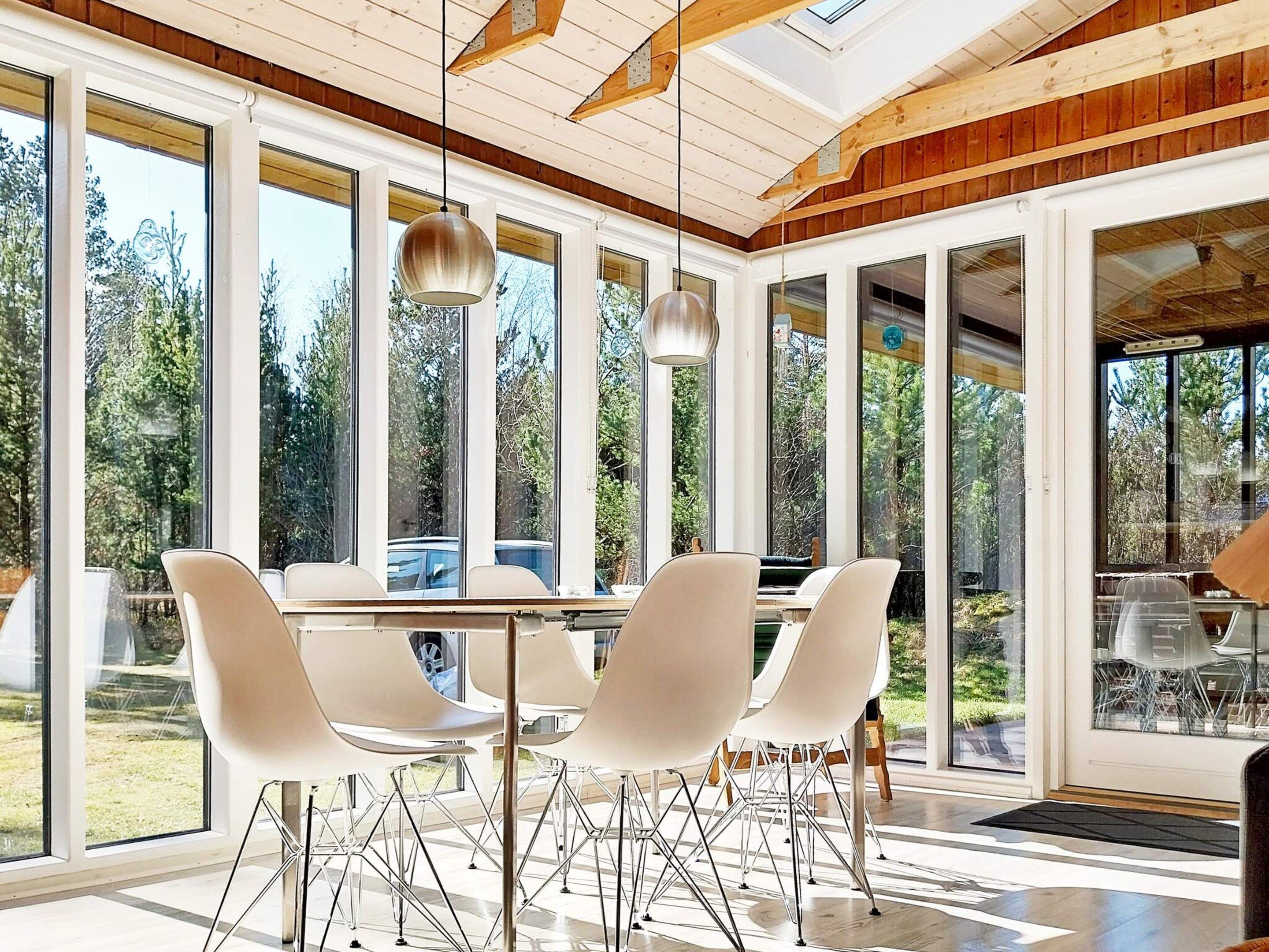 Een moderne eetruimte met een grote tafel en stoelen, grote ramen en een houten plafondconstructie.