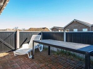 A patio with a table and two chairs, a wooden fence, and a house in the background. - Quaint Holiday Home in Harboøre Jutland near Sea (Harboore)