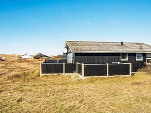 A single-story building with a dark exterior, a sloped roof, and a fenced yard. - Quaint Holiday Home in Harboøre Jutland near Sea (Harboore)