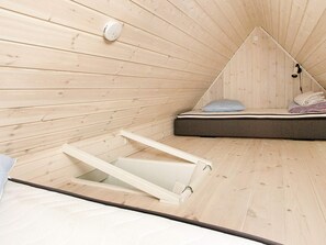A room with a sloped ceiling, a bed with a mattress and pillows, and a small window. - 4 Person Holiday Home in Skagen (Skagen)