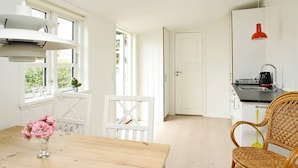 A bright kitchen with white cabinets, a wooden dining table, wicker chairs, and a red pendant light. - 4 Person Holiday Home in Skagen (Skagen)