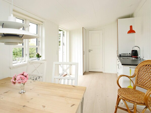 A bright kitchen with white cabinetry, a wooden dining table with a vase of flowers, and wicker chairs. - 4 Person Holiday Home in Skagen (Skagen)