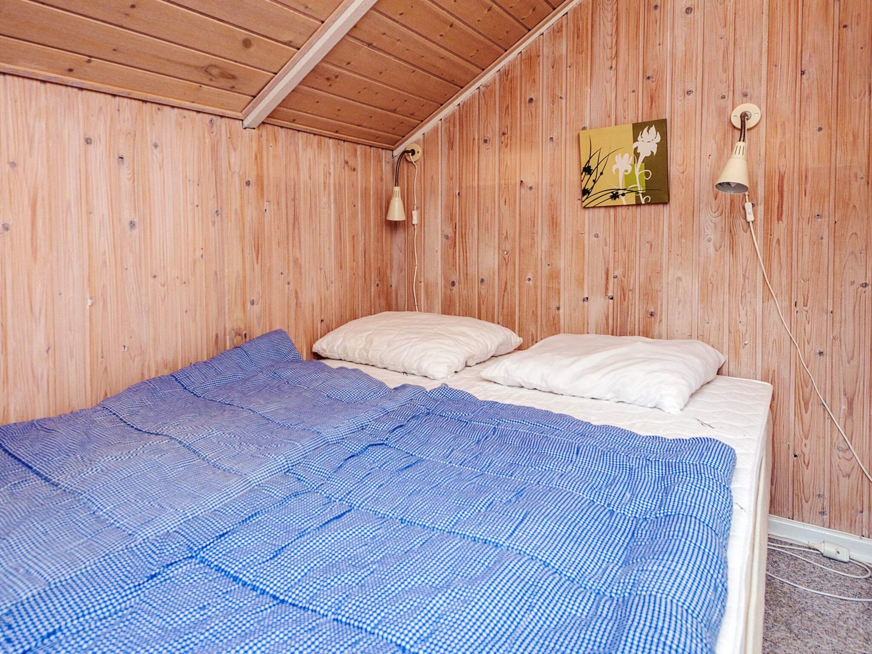 Ein Einzelbett mit blauer Karobettwäsche und weißen Kissen in einem Zimmer mit Holzwänden und schräger Decke.