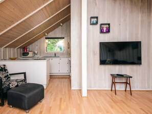 A modern kitchen with a wooden ceiling, a dining area with a black and white patterned chair, and a flat-screen TV mounted on the wall.