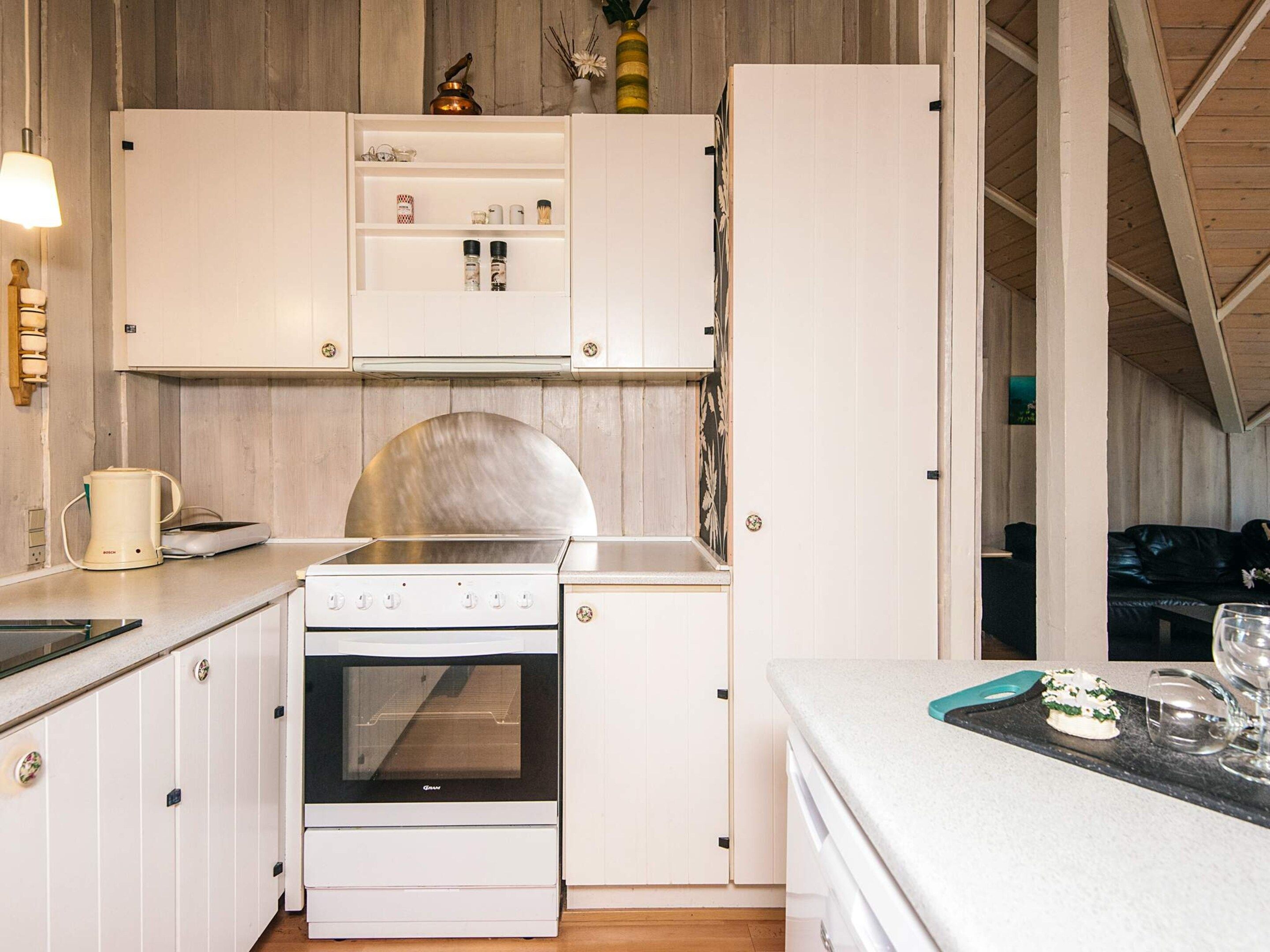 Une cuisine compacte avec des meubles blancs, un four en acier inoxydable et un plan de travail sur lequel se trouvent une bouilloire et des verres.