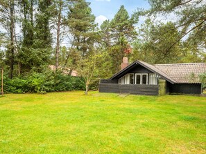 A cabin with a sloped roof, surrounded by a grassy yard and dense trees.
