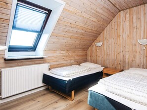 A room with wooden walls, a sloped ceiling, a window with blinds, a bed, a bedside table, and a wall-mounted light fixture. - 3 Person Holiday Home in Ansager (Ansager)
