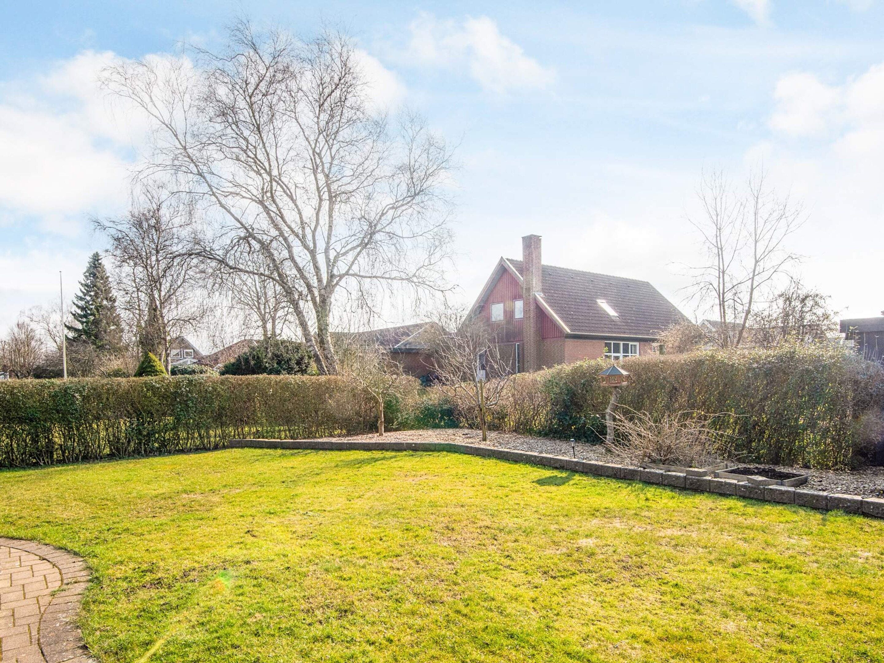 A residential property with a well-maintained lawn, a brick pathway, and a large house with a sloped roof.