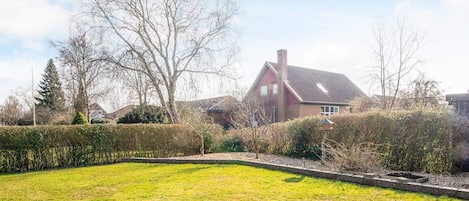 A residential property with a well-maintained lawn, a brick pathway, and a large house with a sloped roof.