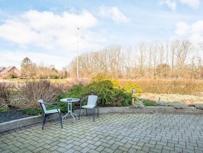 An outdoor patio with a table and chairs, surrounded by a hedge and a parking sign.