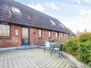 A brick house with a tiled roof, a front door, and a small patio area with a table and chairs. - 3 Person Holiday Home in Ansager (Ansager)