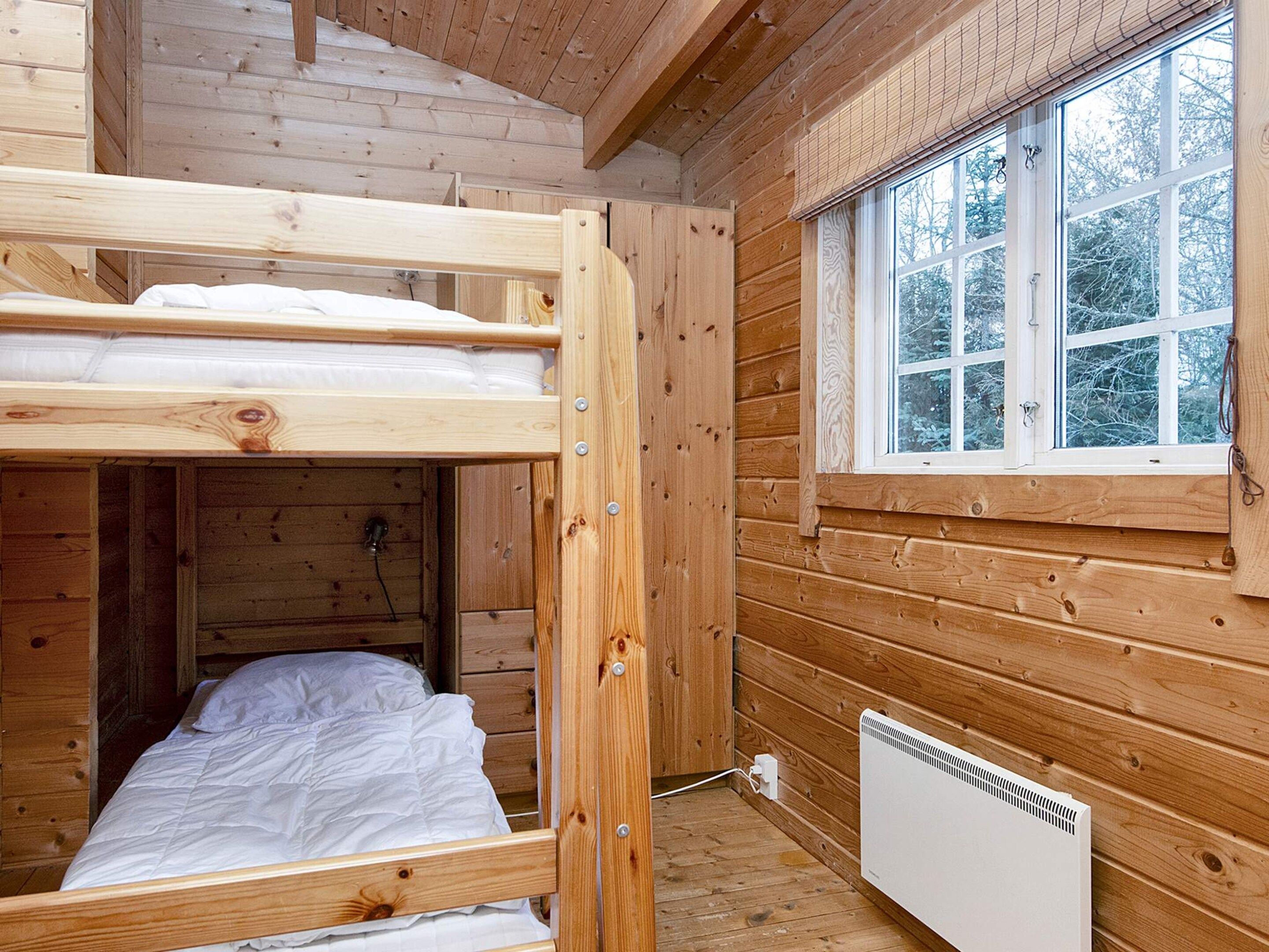 A wooden cabin room with a bunk bed, a window with a view of trees, and a white radiator.