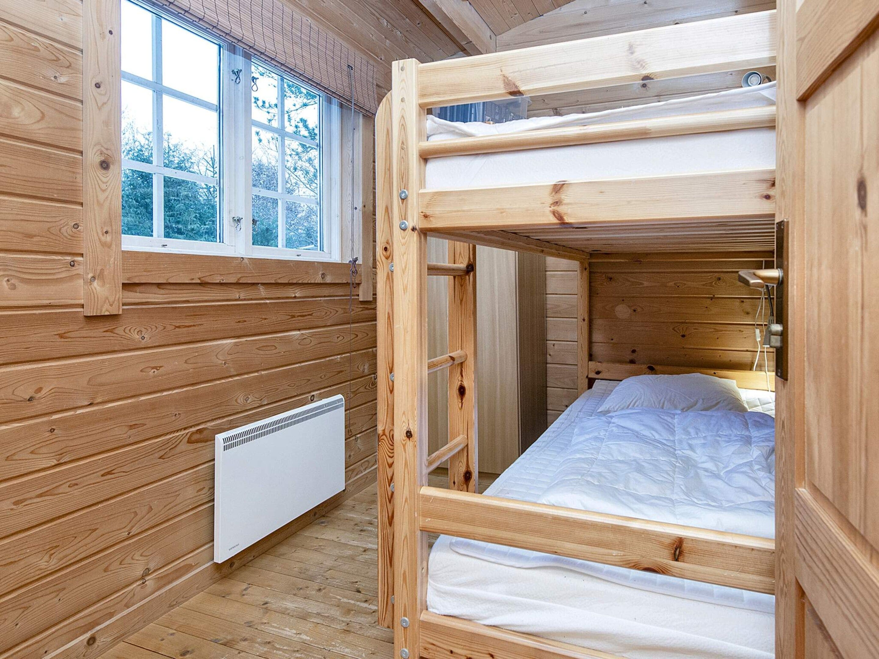 Habitación con literas de madera, ventana, radiador y mesita de noche.