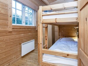 A wooden bunk bed room with a window, a radiator, and a bedside table.