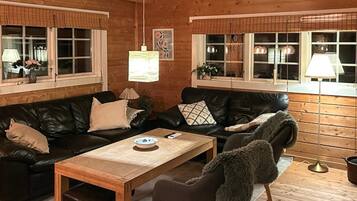 A cozy cabin interior with a wooden interior, a black leather sofa, a wooden coffee table, and a window with a view.