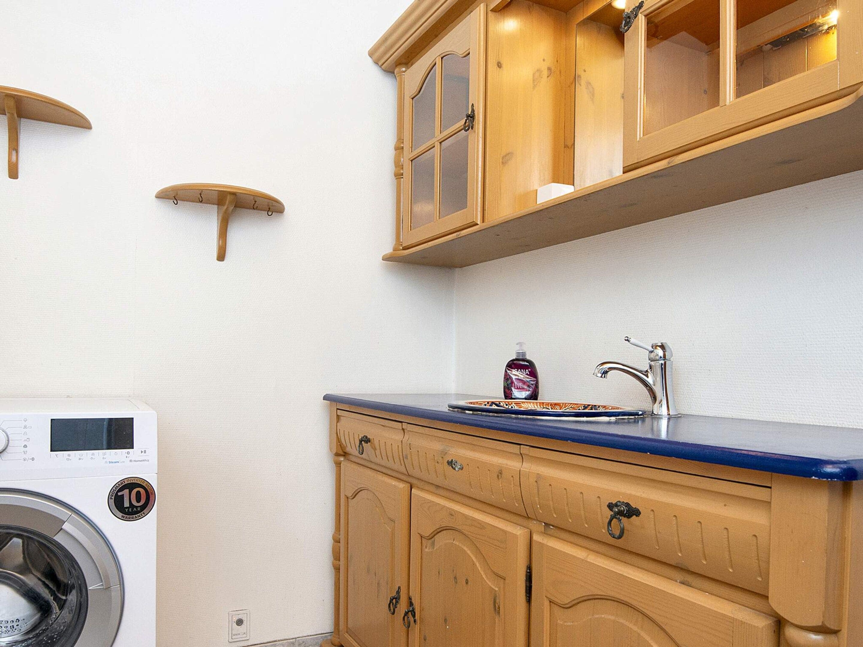 Una cocina compacta con armarios de madera, lavadora integrada y un lavabo con grifo.