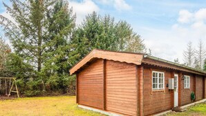 A wooden cabin with a single door and window, surrounded by a grassy yard and trees. - 6 Person Holiday Home in Farvang (Farvang)
