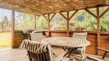 An outdoor wooden deck with a thatched roof, a round table, and two chairs.
