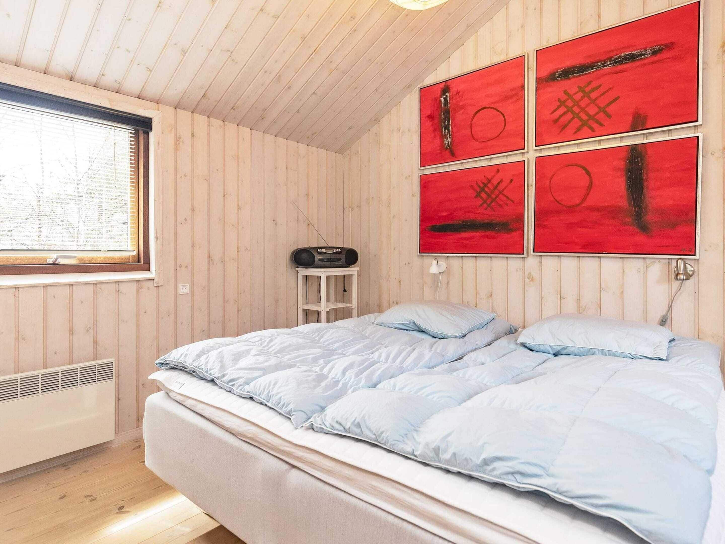 A bedroom with a bed, a window, a radiator, and a radio on a small table.