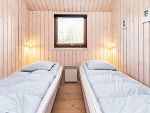 A cabin with two single beds, a window with blinds, and wall-mounted lights.