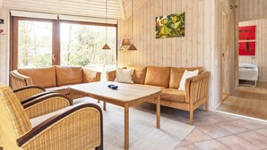 A cozy room with a wooden ceiling, a sofa, a table, and wicker chairs.