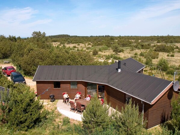 Une cabane en bois avec un toit en pente, une terrasse avec des meubles d’extérieur et une voiture garée à proximité.