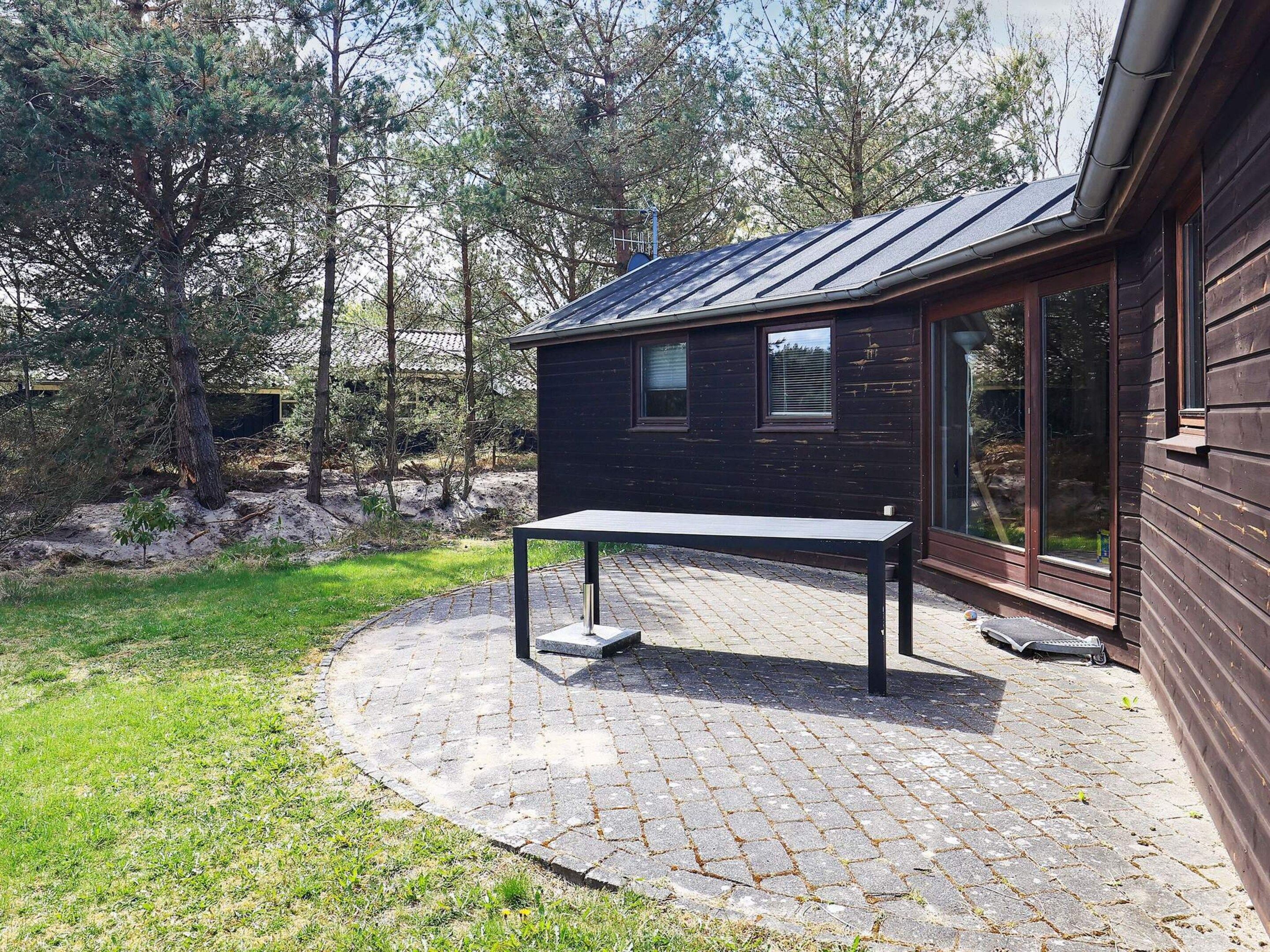 En træhytte med en fliseterrasse og et bord.